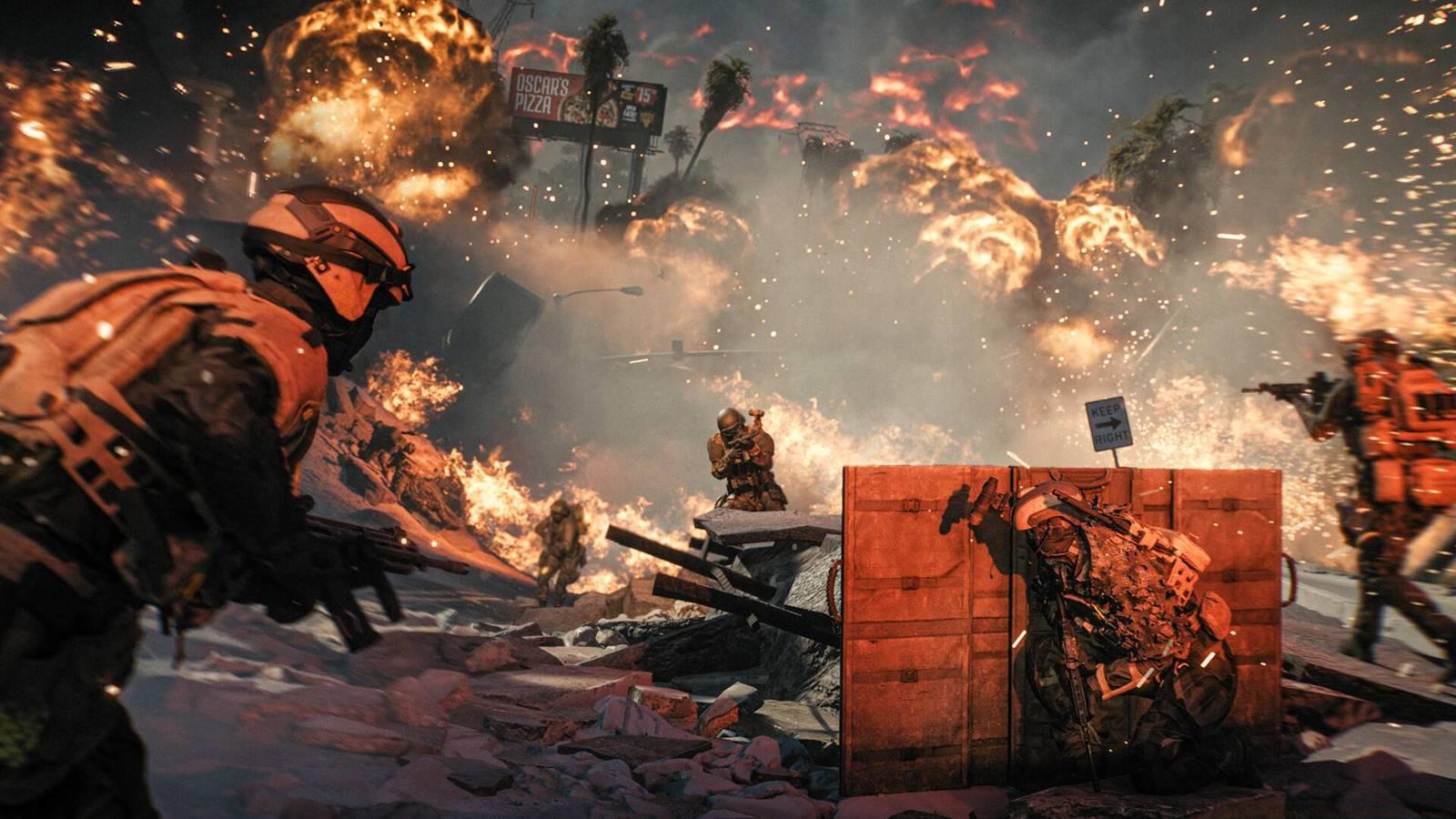 A firefight in Battlefield Redsec, with one soldier hiding behind a barricade and enemies advancing in front of explosions.